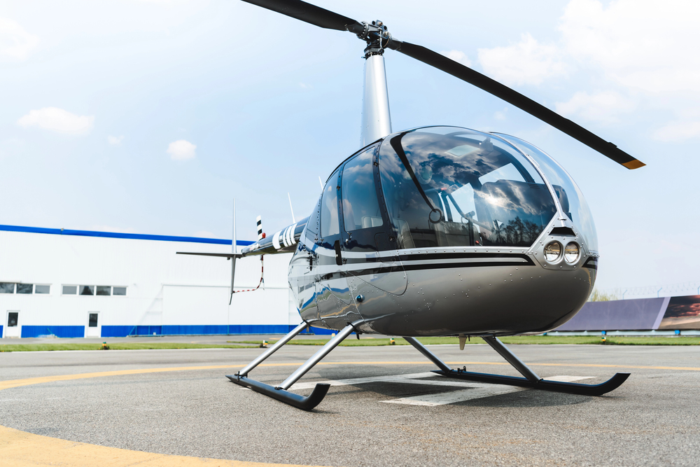 Small airplane parked on a concrete apron near a beige hangar and office building, with a fuel truck and cars in the background at a rural airfield.