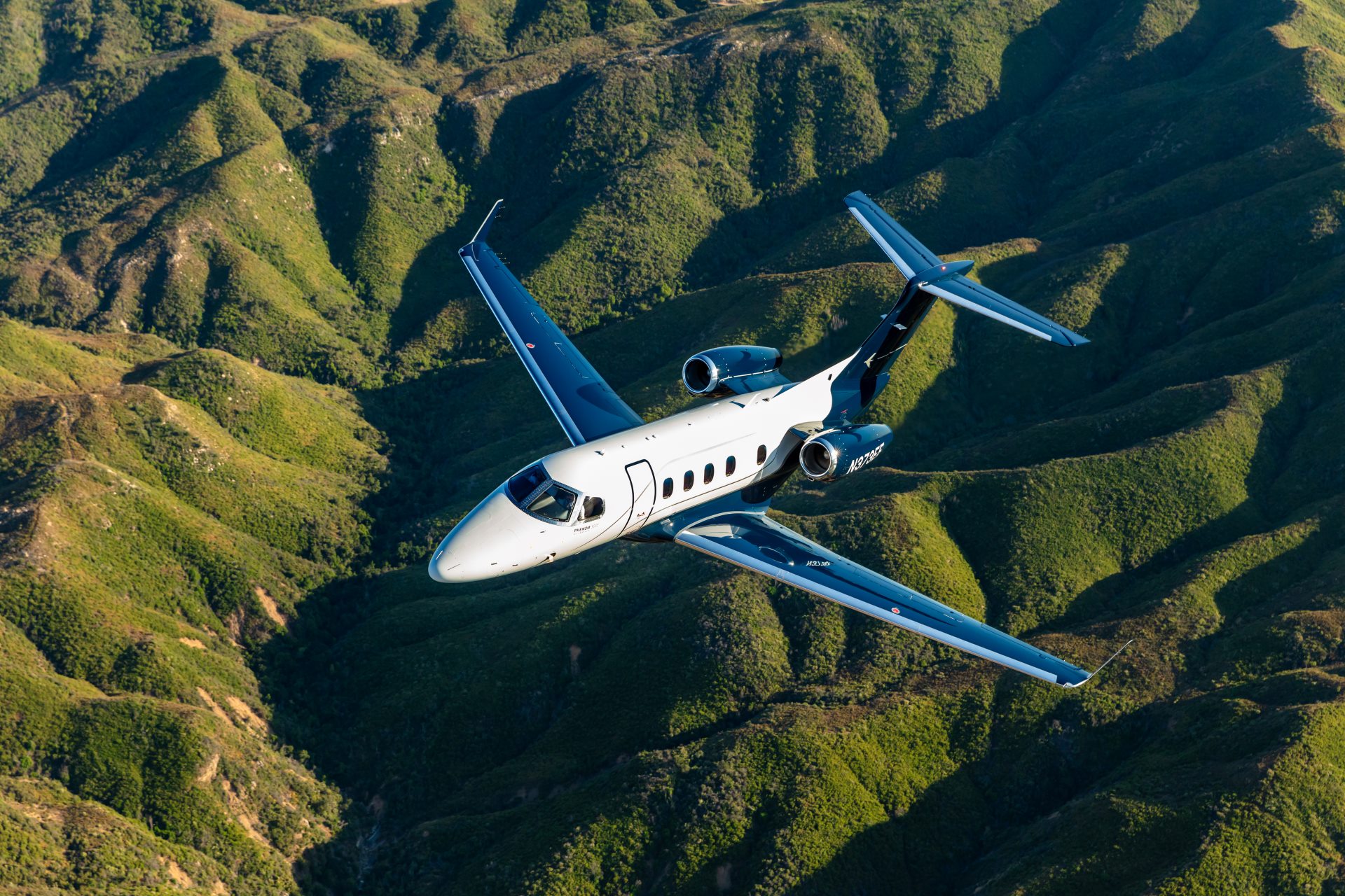 Embraer Phenom 300E in flight over green mountains