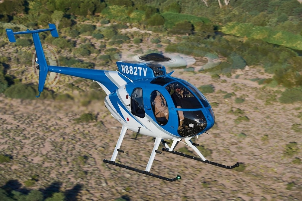 MD 530F helicopter in flight over scrubland